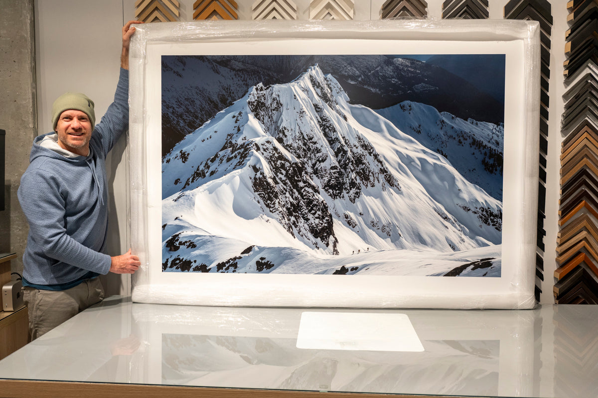 Mike Crane holding a large framed mountain print in the framing shop