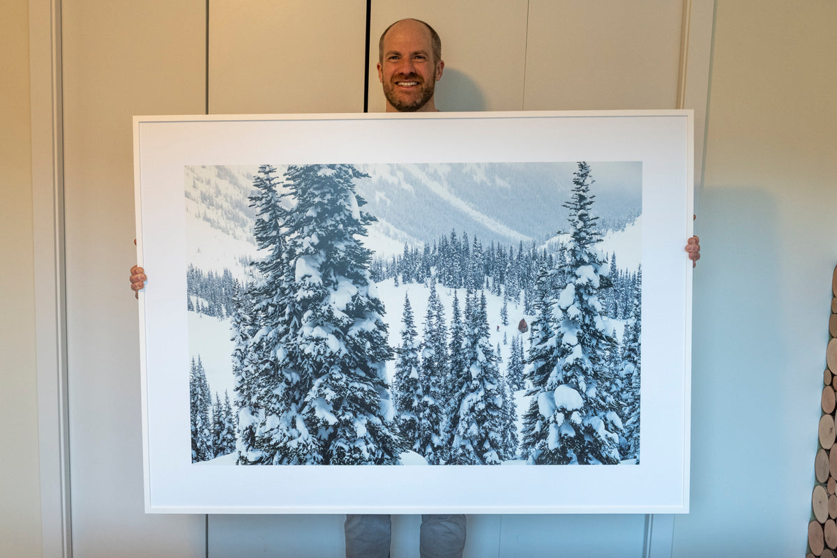 Mike Crane holding a large white-framed black and white print of snowy trees